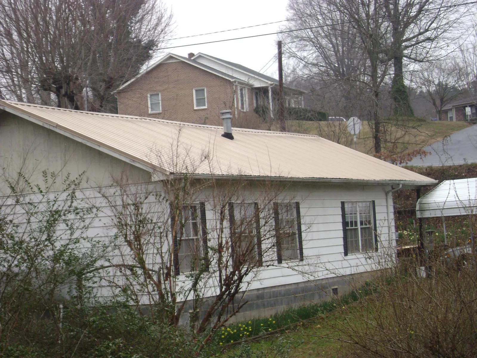 Tan metal roof on a white sided house set into a hillside — Commercial Roofing by Roofing Brothers in Palm Beach
