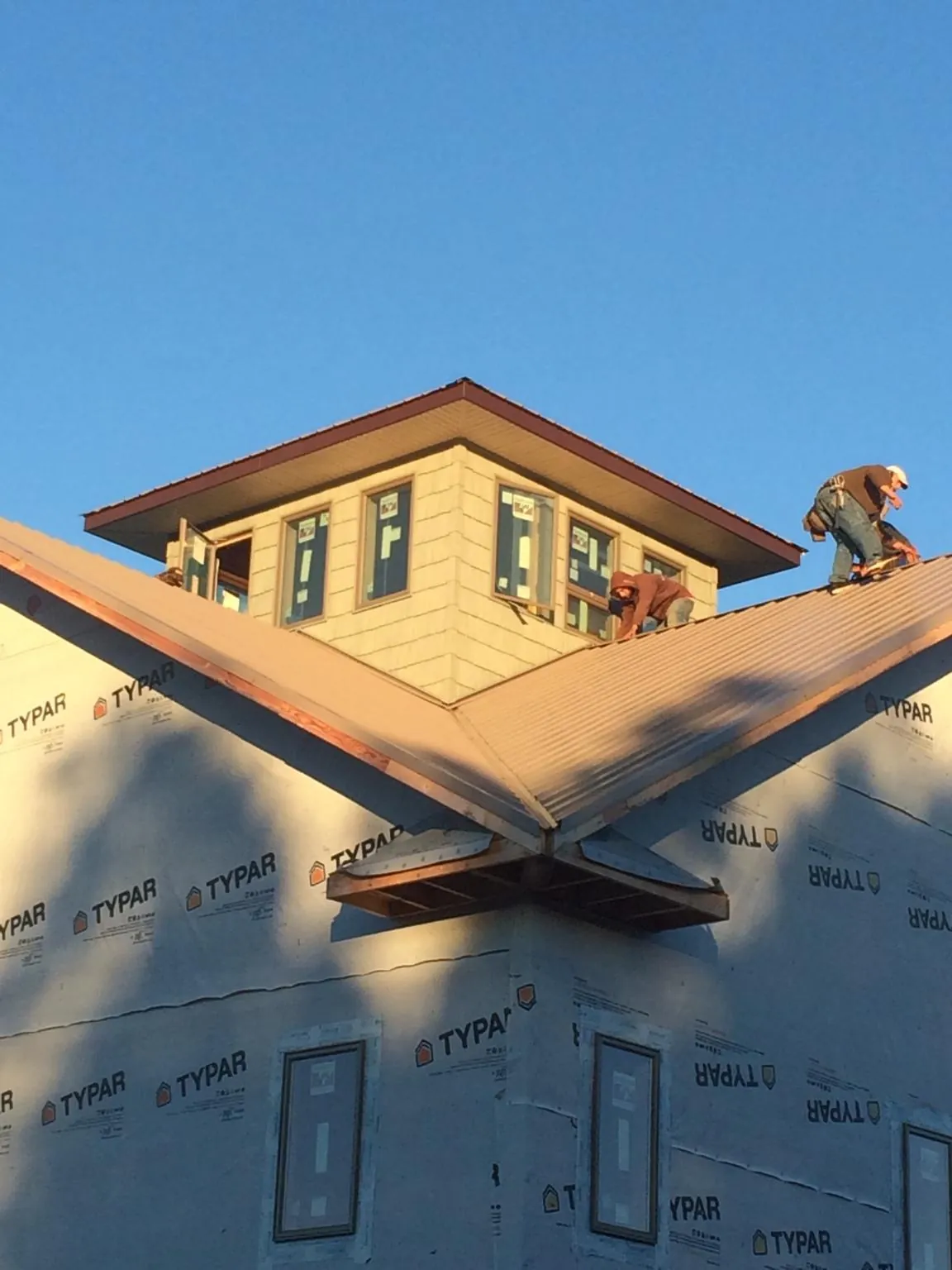 Roofers working around a rooftop cupola on a new metal roof at sunset — Roof Waterproofing in Palm Beach by Roofing Brothers